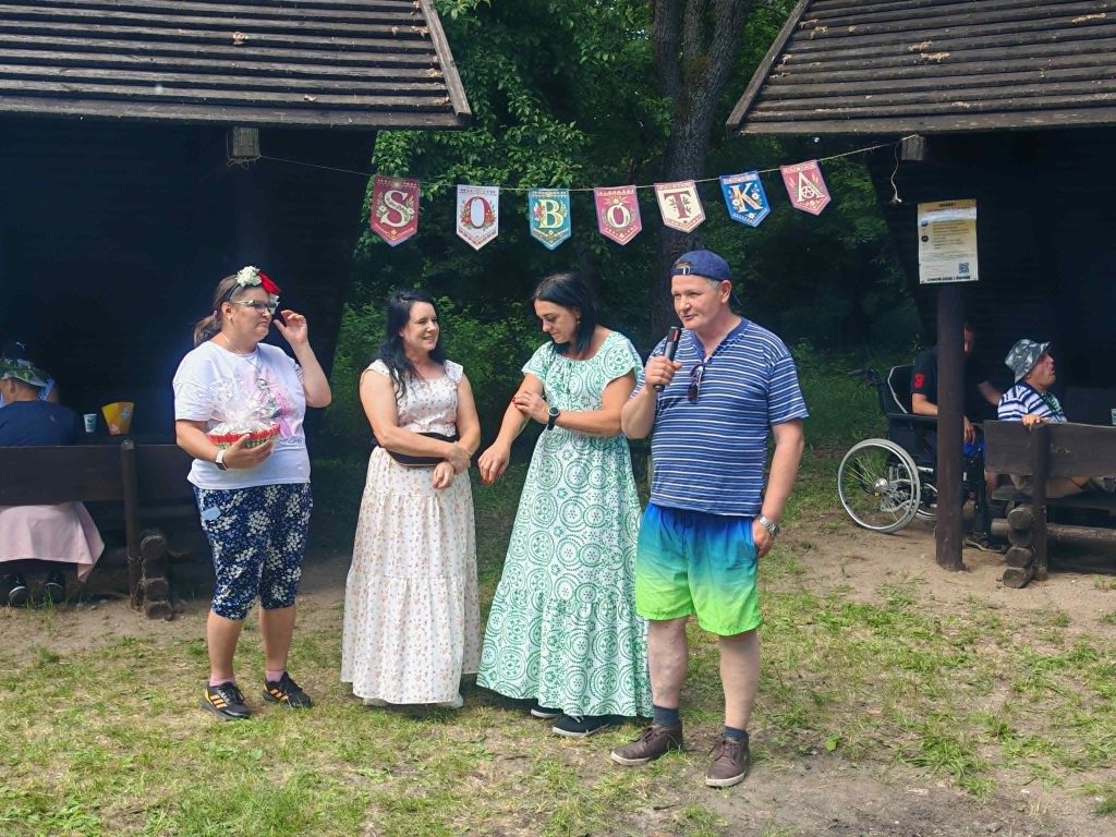 Uczestnicy spotkania stoją pod banerem „Sobótka”, jeden z nich przemawia do zebranych przez mikrofon.