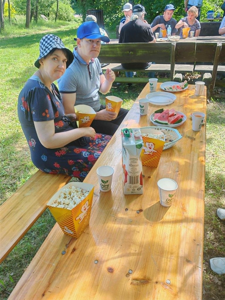 Uczestnicy pikniku siedzą przy drewnianym stole i wspólnie jedzą popcorn.
