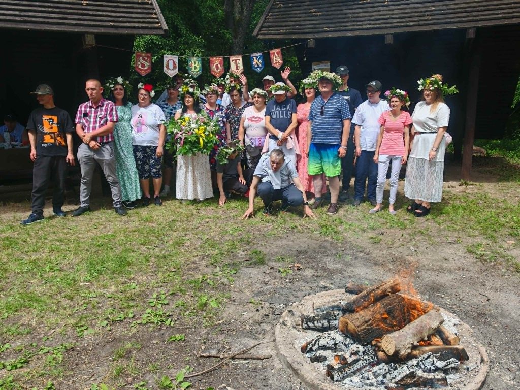 Grupowe zdjęcie uczestników plenerowego spotkania z własnoręcznie wykonanymi wiankami pod banerem „Sobótka” oraz przy ognisku na którym będą pieczone kiełbaski.