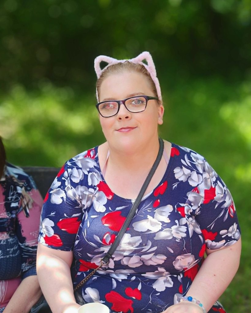 Uczestniczka pikniku sobótkowego w kwiecistej sukience i opasce z uszkami siedzi na ławce na świeżym powietrzu