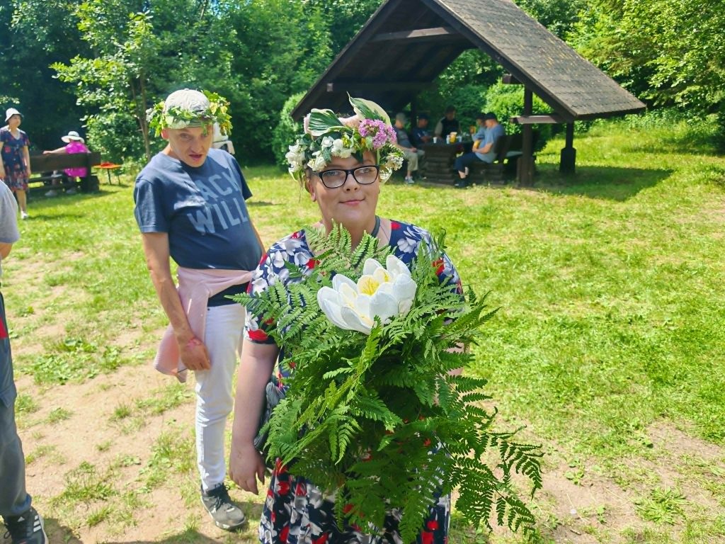 Uczestniczka pikniku pozuje do zdjęcia w wianku oraz z bukietem, który wyróżnia duży biały kwiat