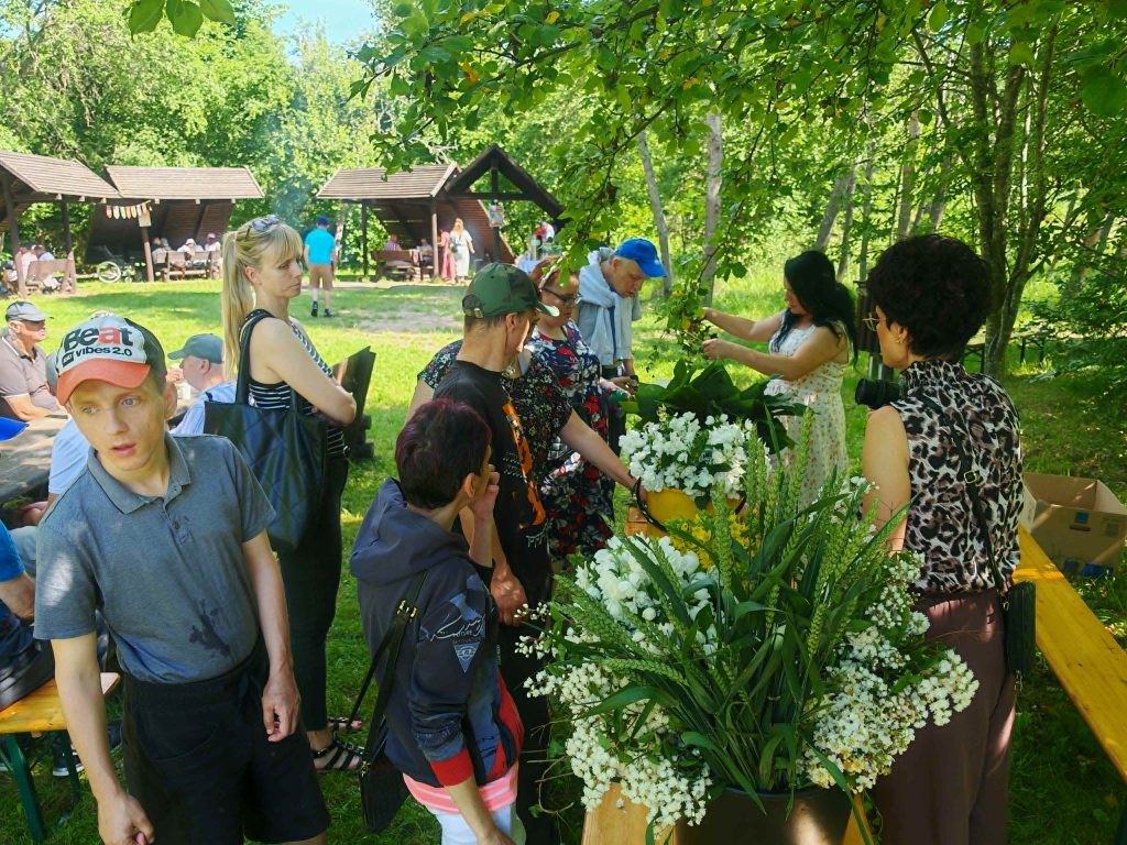 Uczestnicy pikniku wspólnie podchodzą do stołu z kwiatami żeby zrobić wianki
