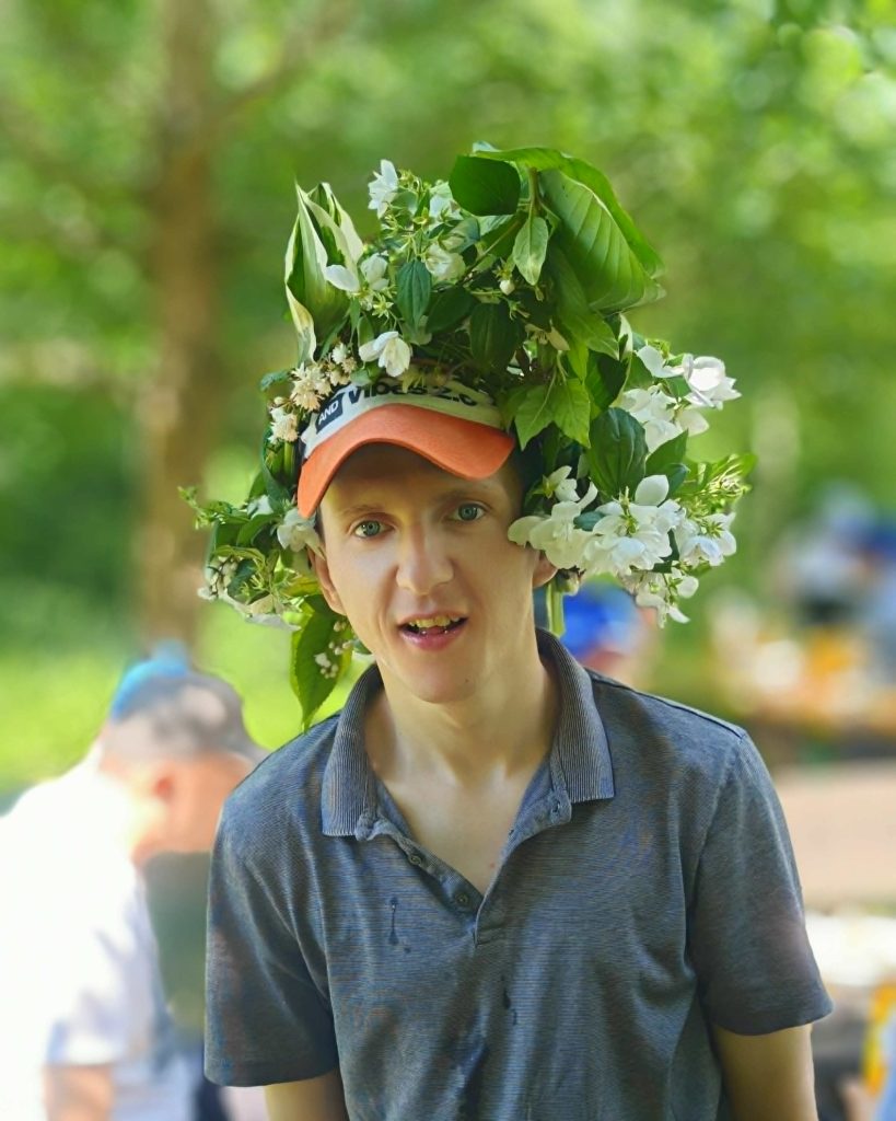 Uczestnik pikniku pozuje do zdjęcia w założonej na głowie kompozycji kwiatowej.