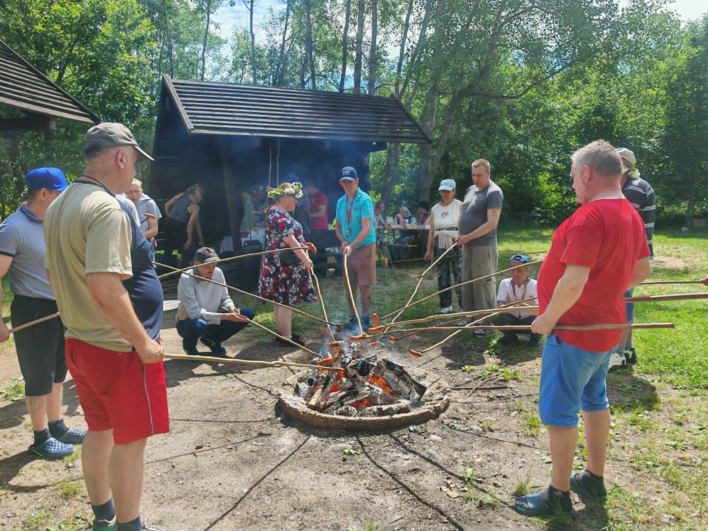 Uczestnicy pikniku wspólnie pieką kiełbasy przy ognisku.
