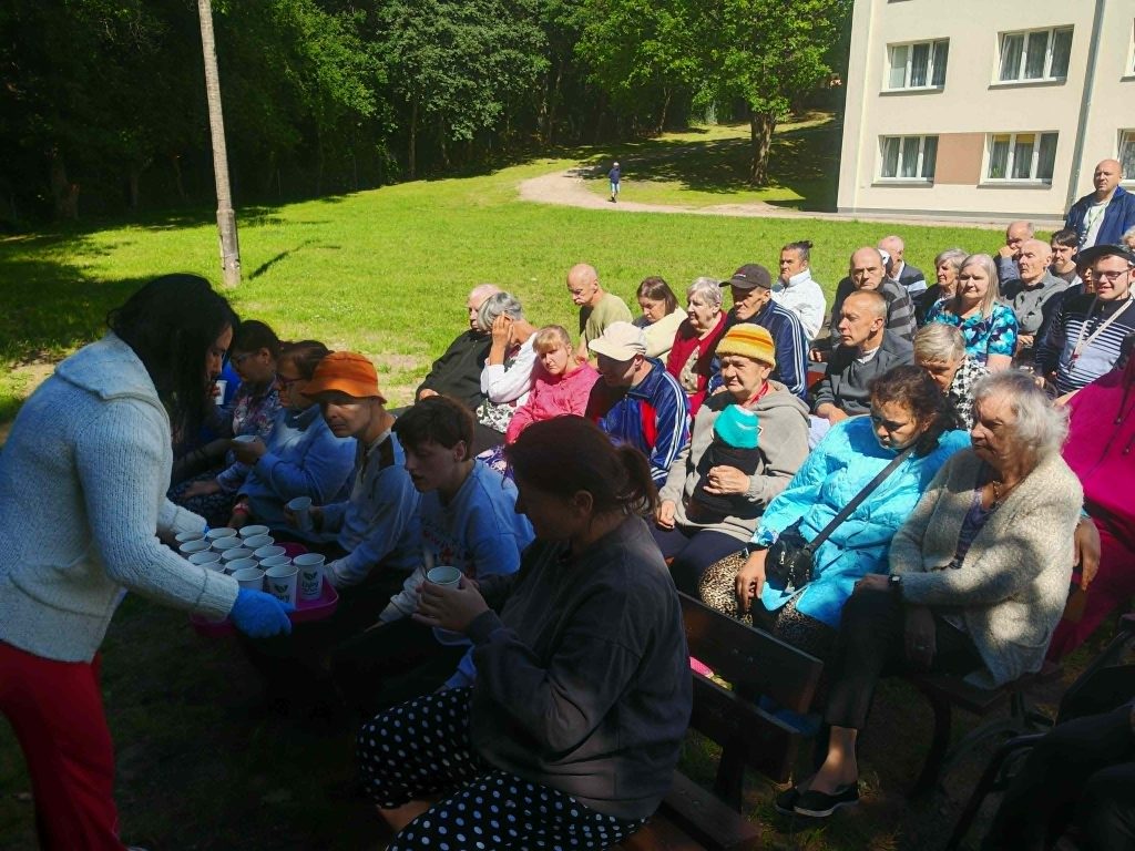Pracownica DPS Żydowo rozdaje mieszkańcom ciepłe napoje podczas kina plenerowego zorganizowanego na terenie ośrodka.